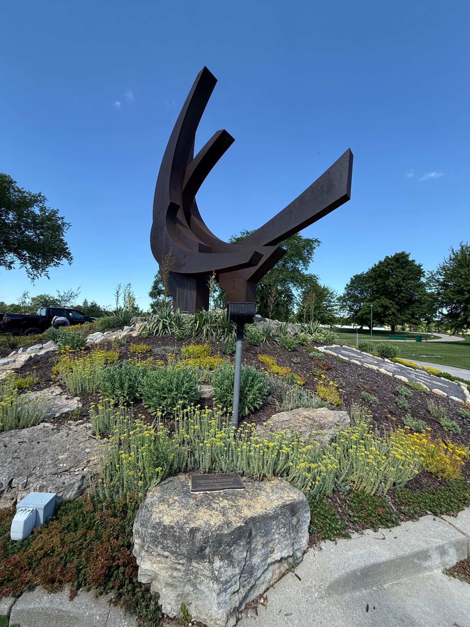 O.V. Shaffer's large rust-colored steel sculpture Celebration rising above the plantings at Riverside Park in Beloit