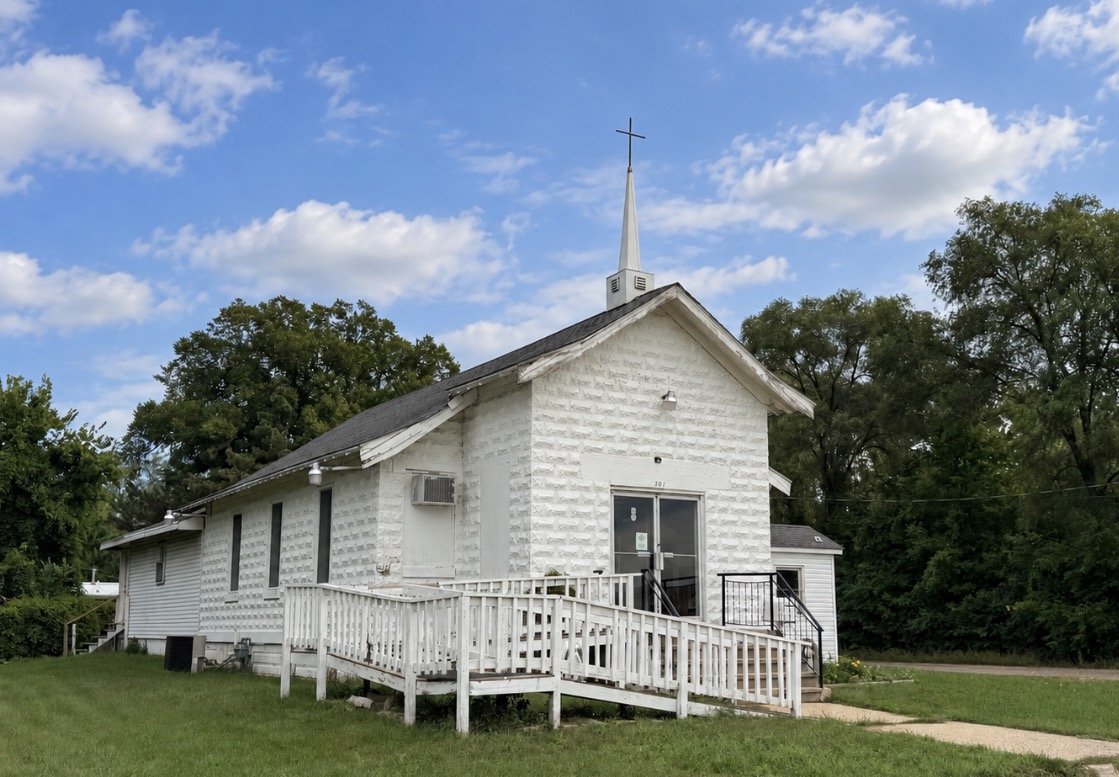 The small white church at 207 Olympian Boulevard beneath a blue sky